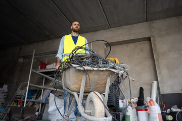Construction worker transporting cables in a wheelbarrow