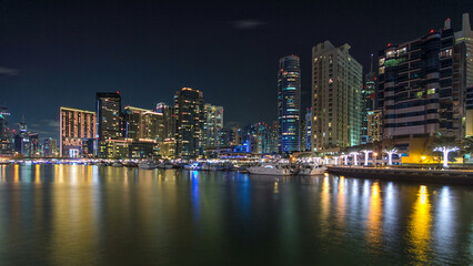 Fototapeta premium Dubai Marina towers and yachts reflected in water of canal in Dubai day to night timelapse