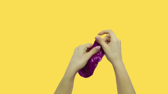 hands stretching and squishing vibrant purple slime against a yellow background
