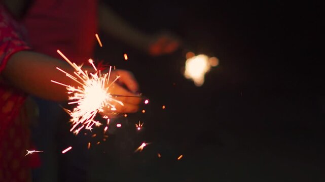 Close up shot of children hands holding sparklers and celebrating New Year during night. Happiness and liveliness during Christmas holidays. People enjoying festival. Diwali firecracker background.