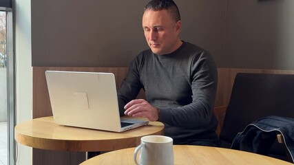 Late worker typing computer taking coffee sip sitting office desk closeup. Bearded confident corporate employee looking screen flipping documents at workplace. Serious businessman doing laptop.