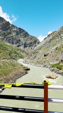 4K Vertical shot of flowing river in mountain as seen from bridge in Lahaul, Himachal Pradesh, India. Beautiful nature background. View of Chenab river flowing in Himalayas as seen from moving vehicle