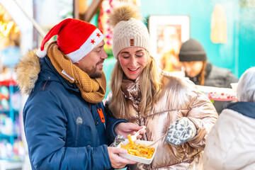 Cheerful couple enjoying delicious food at a Bavarian Christmas market in Germany glowing with warm winter lights