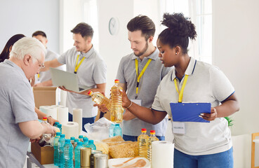 Diverse volunteers group sorting donations of foodstuffs in cardboard boxes for charity food drive. Mature and young people volunteering in food bank working in charitable foundation together.