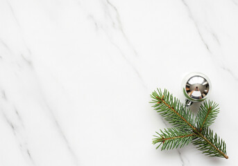 Minimalist festive arrangement featuring a fresh fir branch and a shiny silver ornament, elegantly displayed on a clean white marble background, ideal for seasonal greetings and winter holiday designs