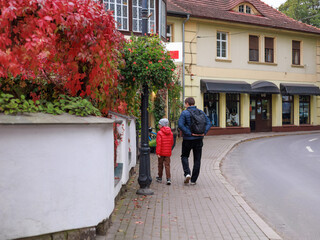 A family walks together along a curved street lined with autumn colors and open copy space. Concept of movement, family journey, everyday exploration and seasonal travel.