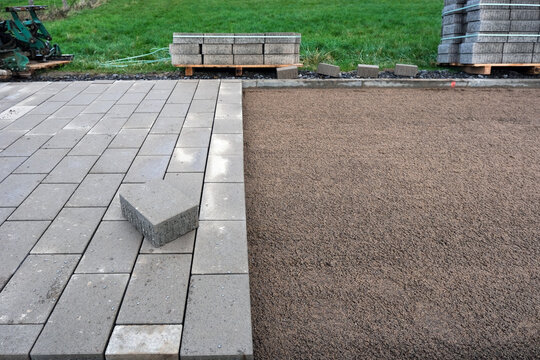 Seitliche Nahaufnahme von Pflasterarbeiten an einem Rad- und Gehweg mit verlegten Steinen, Sand, Werkzeugen und angelieferten Pflastersteinen in l&auml;ndlicher Umgebung, viel Copy Space