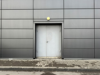 A gray wall features a plain door with a yellow light above it in a city setting
