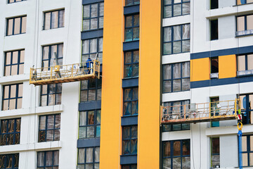 Construction worker on elevated suspended platform fit glass windows onto the towering residential building, precision facade installation. Worker on lift platform work at height, installing window