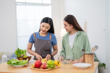 Two women prepare food together in a bright kitchen while sharing smiles and conversation on a sunny day