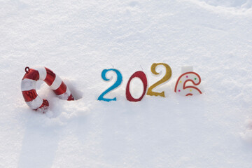 Candles - numbers, and Christmas tree decorations are buried in white snow and form the inscription 2026. The concept of New Year and Christmas