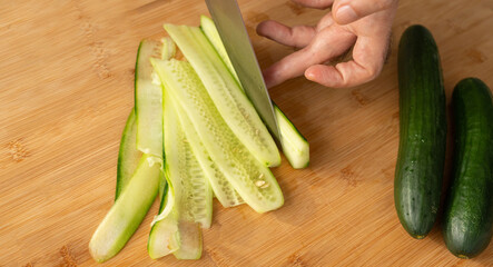 Slicing cucumbers with a large knife on wood cooking board close-up