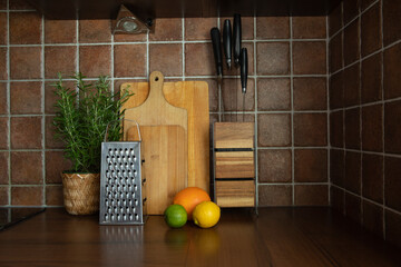 Kitchen countertop with cutting boards, metal grater, fresh citrus fruits and potted rosemary herb against tiled backsplash. Cozy home kitchen interior with natural light and cooking accessories.