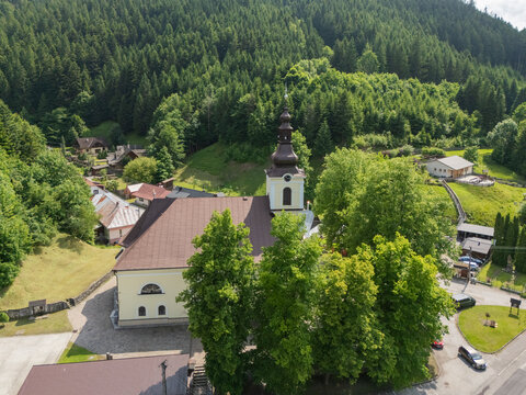 Aerial view of the church steeple piercing the skyline amidst the verdant trees, casting shadows on the roofs of Stare Hory, Stare Hory, Banska Bystrica Region, Slovakia.