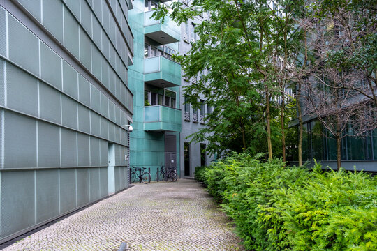 Urban pathway bordered by modern architecture and greenery, blending geometric forms, outdoors minimalism, perspective, structure and design into a quiet open space