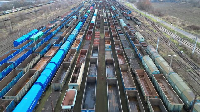 Aerial view of a vast freight train yard showcasing rows of colorful train cars, with a gradual zoom out revealing the expansive layout and intricate details of the scene
