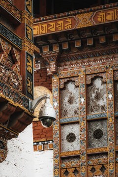 View of intricate, colorful patterns adorn the walls, a modern security camera contrasts with the ancient architecture, Punakha, Bhutan.