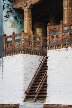 View of a wooden staircase ascending to a temple, adorned with intricate carvings and white walls, inviting contemplation and reverence, Punakha, Bhutan.