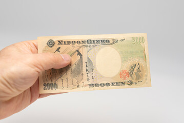 Hand holding a rare Japanese 2,000 Yen banknote (Nippon Ginko) on a white background. Japan economy and finance concept.