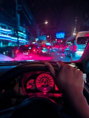 Night city traffic view from inside car with neon lights and driver&rsquo;s hand on steering wheel