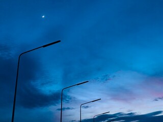 A serene twilight sky with a soft gradient from deep blue to pastel pink, featuring a bright crescent moon above a quiet landscape.