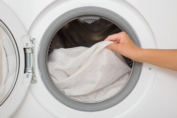 Young adult woman hands holding and unloading white day transparent curtains from opened washing machine. Delicate fabric care. Closeup. Font view.