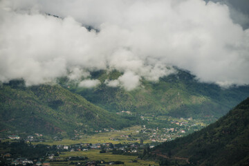 View of a vibrant valley nestled amidst lush green mountains, partially veiled by ethereal clouds, creating a serene and awe-inspiring landscape, Paro, Bhutan.
