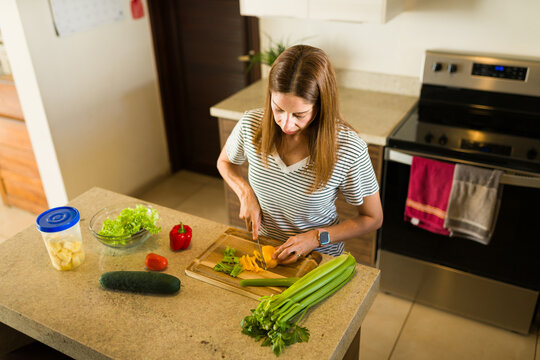 High angle view of a woman chopping fresh vegetables for a healthy salad on a kitchen countertop, preparing a nutritious meal - Powered by Adobe