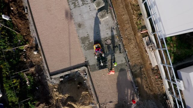 Top down view as construction crew lays concrete pavers, using compaction machines and tools to build durable sidewalks in commercial development.