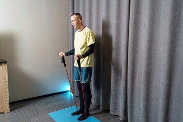 A man warms up his muscles using a resistance band. Fitness workouts at home with a resistance band. Strong muscles and a healthy body through physical exercise.