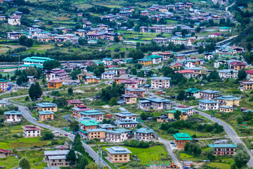 Aerial view of clustered buildings nestled amidst verdant hills, where rooftops echo the earth tones, creating a harmonious blend of architecture and nature, Haa Valley, Bhutan.