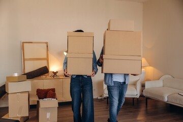 No faces visible, standing. A couple carrying cardboard boxes while moving into a new apartment