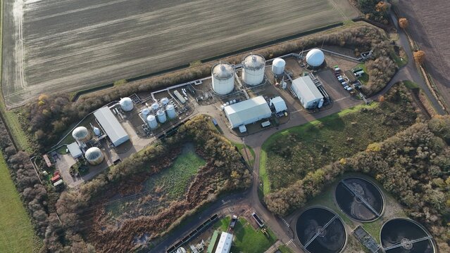 Aerial view of a sprawling industrial plant nestled amidst fields and round structures, a network of pipes weaving through, Kings Lynn, United Kingdom.