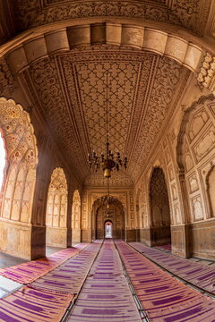 View of ornate arches and ceilings adorned with intricate patterns, casting shadows on the purple carpets in Badshahi Masjid Mosque, Lahore, Lahore, Pakistan.