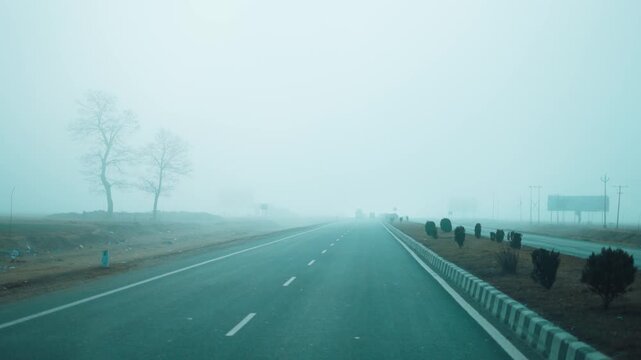 4K shot of mountain road in foggy winter morning at Kashmir, India. Dry trees and heavy fog on sides. POV shot of car driving on dreamy mountain road. Roadtrip and travel concept.