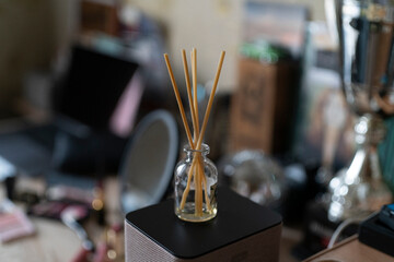 Reed sticks stand in a glass bottle on a table surrounded by various objects and tools
