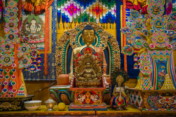 View of golden Buddha statue glows, surrounded by vibrant offerings and intricate decorations in a sacred space, Paro, Bhutan.