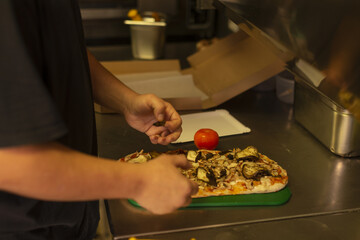 hands arranging mushroom and tomato pizza, garnished with herbs on green tray for pickup, rustic crust and visible topping