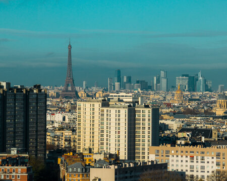 Aerial view of the Eiffel Tower piercing the skyline amidst a sprawling cityscape of varied architectural styles, bathed in the soft glow of a winter afternoon, Paris, Ile-de-France, France.
