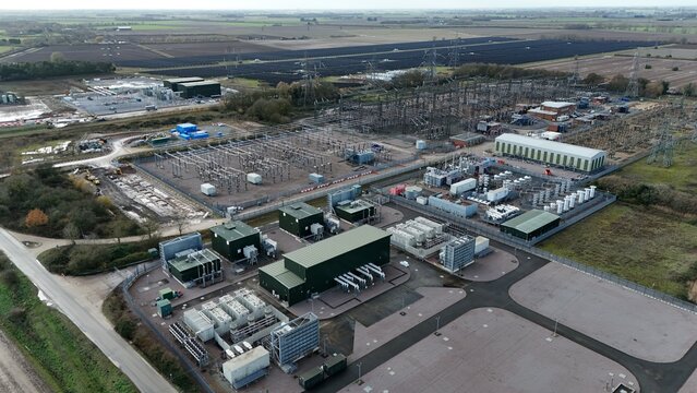 Aerial view of a modern industrial landscape with a complex of buildings and electrical infrastructure contrasting against the flat, arable fields, Sutton Bridge, United Kingdom.