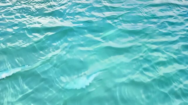Close-up of crystal clear, light turquoise blue water gently rippling under the sun, creating beautiful light caustics on the surface.