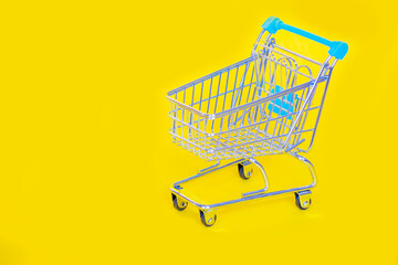 Mini shopping cart on a bright yellow background, symbolizing retail, e-commerce, and consumer shopping.