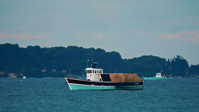 A wooden workboat with a brown tarp cover anchored on a windy sea