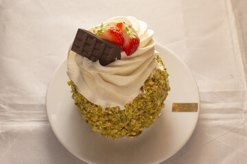 top view pistachio cake with chocolate square and strawberry, crushed nut coating and velvety cream swirl, rich color contrast