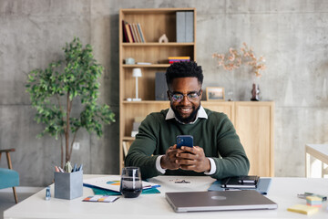 African american man smiling using smartphone in modern office