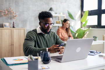 African american man using smartphone while working in modern office