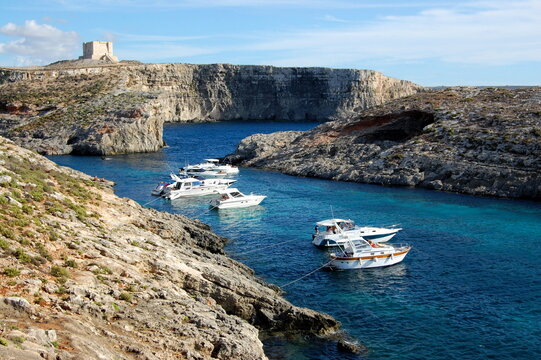 Boats are in the Blue Lagoon in Comino, Malta. St Mary's Tower is seen  in the distance.