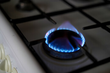 Close-up of a lit blue gas burner on a modern white stove, highlighting energy consumption and...