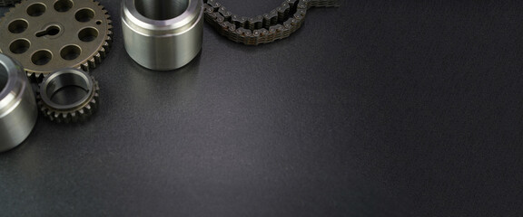 Metallic gears, bushings, and chain components arranged in the corner of a dark, textured background with ample copy space.