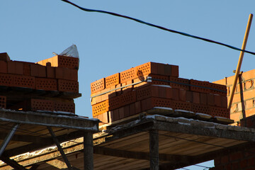 Stack of Red Bricks on an Unfinished Construction Site Against a Clear Blue Sky